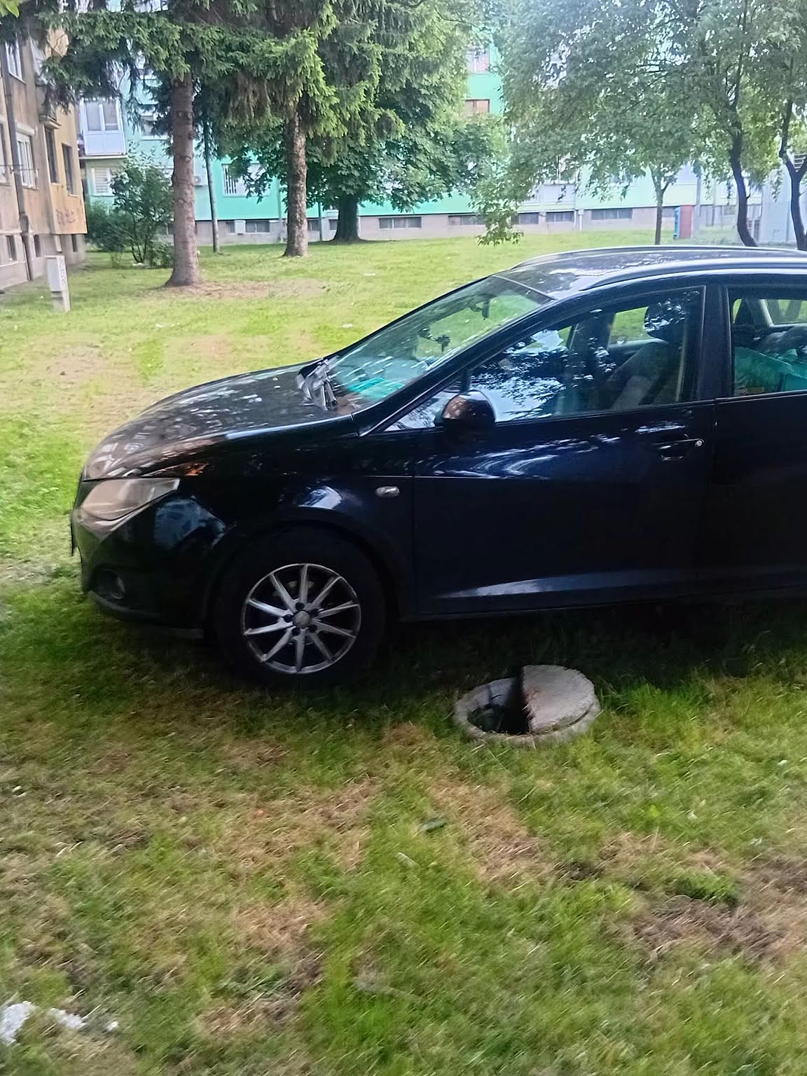 Automobil parkiran na zelenoj površini pored otvorenog šahta, primjer problema za prijavu